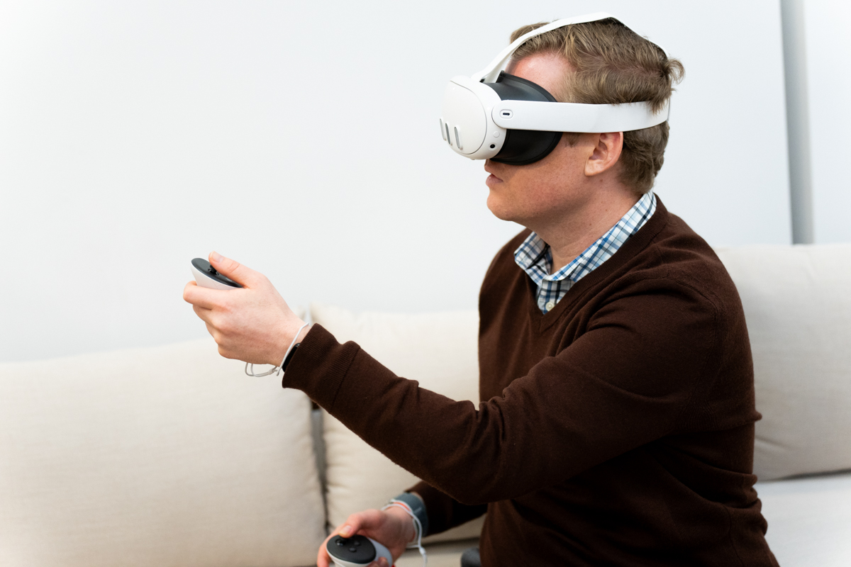 Side view of a man wearing a Meta Quest 3 mixed reality headset and holding a controller.